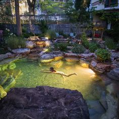 a person swimming in a pool surrounded by rocks and plants at night with lights on