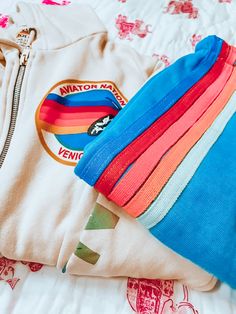 a rainbow colored zippered hoodie laying on top of a bed next to a white t - shirt