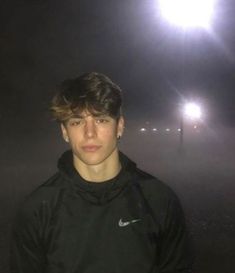 a young man standing in front of a street light on a foggy night with his head turned to the side