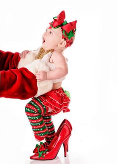 a baby dressed up as santa claus is being held by a man in red shoes