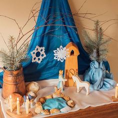 a nativity scene is displayed on a table with candles and other decorations in front of a blue drape