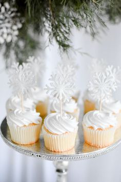 cupcakes with white frosting and snowflakes on them sitting on a silver tray