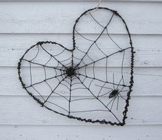 a metal heart shaped like a spiderweave hanging on a white wooden wall with black wire