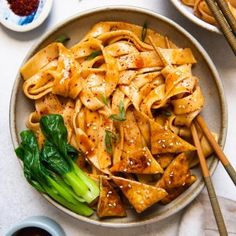 a bowl filled with noodles and vegetables next to chopsticks on a table top