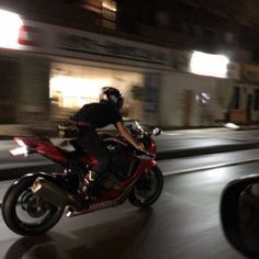 a man riding on the back of a red motorcycle down a city street at night