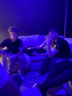 three people sitting on a couch playing video games in a room with blue lights and purple lighting