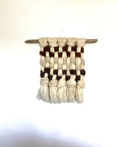 a wall hanging made out of white and brown yarn with a piece of wood sticking out of it