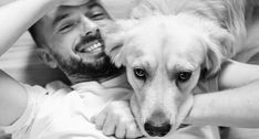 a man laying on top of a bed next to a white dog with his head under his arm