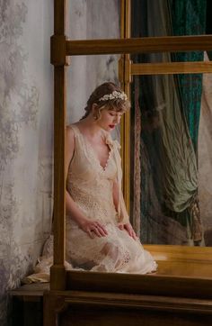 a woman sitting on top of a bed in front of a mirror wearing a dress