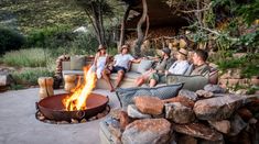 four people sitting around a fire pit in the middle of a yard with large rocks