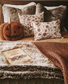 a bed topped with lots of pillows next to a book and a jack - o'- lantern