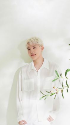 a young man standing in front of a white wall with green leaves on the side