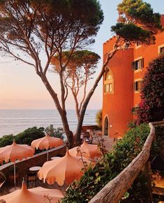 an outdoor dining area with umbrellas and tables overlooking the ocean at sunset or sunrise