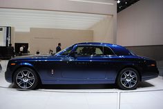 a blue rolls royce on display in a showroom with people looking at the cars