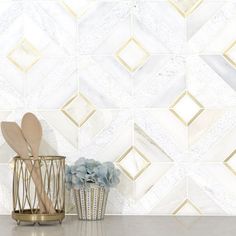 a white and gold tiled wall with some utensils on it next to a vase