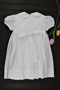 This classic dress is perfect for weddings, christenings, or blessings. The smocking on the bodice is accented with white pearls. 65% Polyester - 35% Cotton Machine wash 3 Button back closure Classic Dresses With Smocked Back For Daywear, Classic Daywear Dresses With Smocked Back, Solid Fitted Dress For First Communion, Fitted Classic Smocked Dress, Elegant Fitted Baptism Dress With Smocked Bodice, Classic Ruffle Dress For First Communion, Classic Short Sleeve Dress For Baptism, Classic First Communion Dress With Ruffles, Classic Ruffled Dress For First Communion