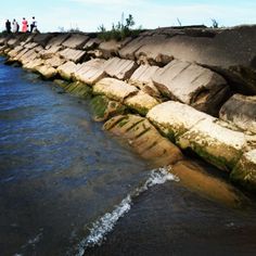 people are standing on the edge of a rock wall by the water's edge