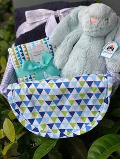 a stuffed animal sitting in a basket on top of some leaves and bushes with other items around it