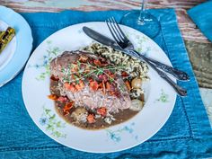 a white plate topped with meat and veggies next to a glass of wine