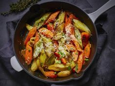 a pan filled with carrots and other vegetables covered in parmesan cheese