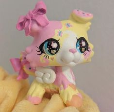 a pink and yellow toy cat with big eyes on top of a stuffed animal teddy bear