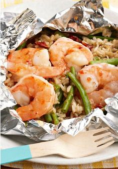 shrimp, green beans and rice in foil on a plate with a fork next to it