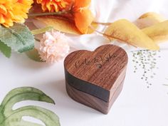 a wooden heart shaped box sitting on top of a table next to flowers and leaves