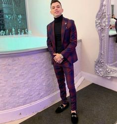 a man standing in front of a mirror wearing a purple suit and black turtle neck sweater