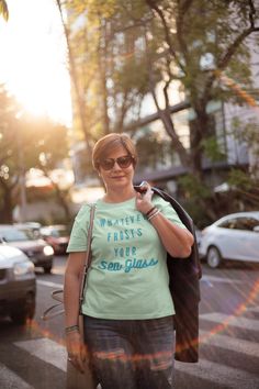 a woman walking down the street with her cell phone up to her ear and wearing a t - shirt that says whatever frosts your son lucas