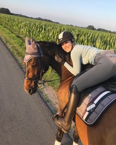 a woman riding on the back of a brown horse next to a lush green field