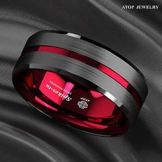 a black and red wedding band with two pink stones in the center on a satin background