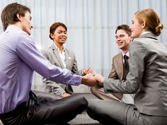 three business people sitting on the floor shaking hands with each other in an office setting