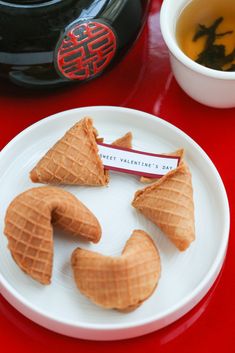 three waffles on a white plate next to a cup of tea and a black teapot