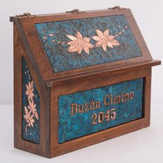 a wooden box that has a blue and gold design on the front with flowers in it