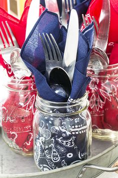 a glass jar filled with silverware sitting on top of a metal tray covered in red, white and blue napkins