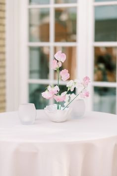 pink flowers in a white vase sitting on top of a table next to a window