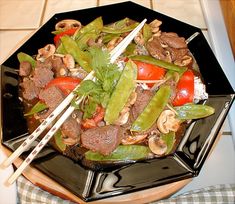 a black plate topped with meat and veggies next to chopsticks on a table