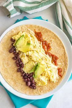 a white plate topped with a tortilla covered in beans and avocado