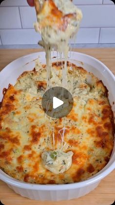 someone is sprinkling cheese on a cheesy casserole in a white dish