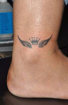 a tattoo on the foot of a person with an angel wing and crown design above it