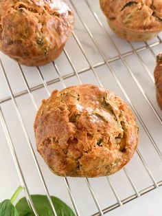 muffins cooling on a wire rack with spinach leaves next to it and another muffin in the background