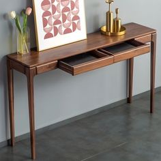 a wooden table with two drawers and a painting on the wall next to it,