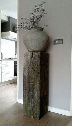 a vase that is sitting on top of a wooden block in the middle of a room