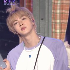 a young man holding a cell phone and wearing a purple shirt with pearls on it