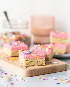 two pieces of cake with pink frosting and sprinkles on a cutting board