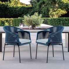 two blue chairs sitting next to each other on top of a cement floor in front of a table