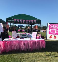 a table covered in pink tulle under a green tent with signs and banners on it