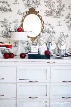 an old dresser with apples on it in front of a wallpapered wall and mirror