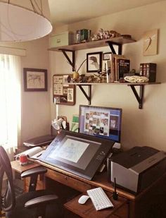 a desk with a computer and printer on it in front of a wall mounted book shelf