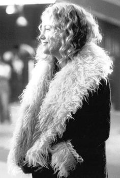 a woman standing on the street talking on her cell phone while wearing a fur coat